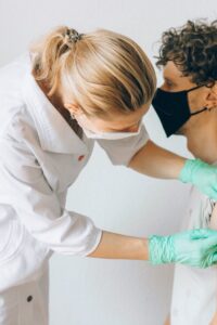 A healthcare worker gives a vaccine shot to a patient wearing a mask, highlighting medical safety and health precautions.